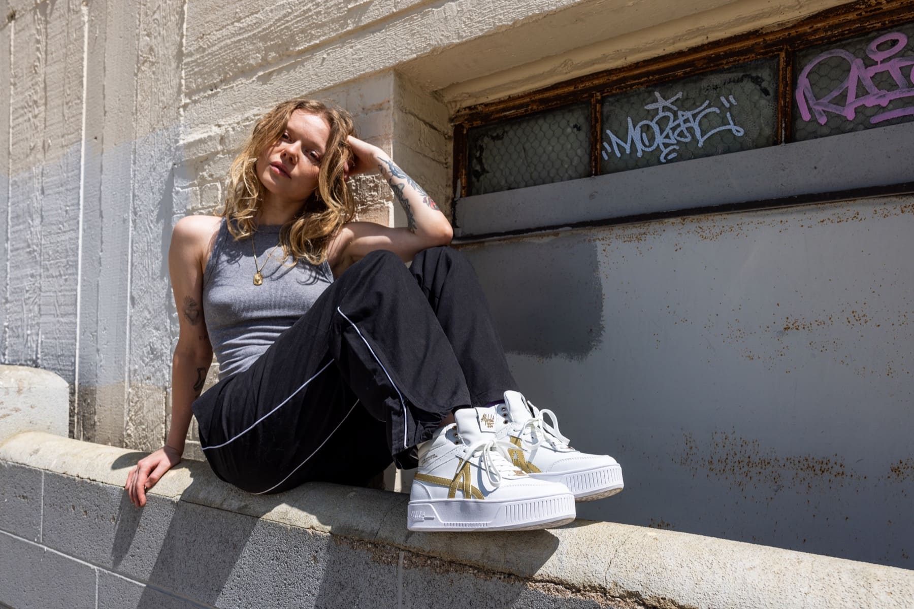 Model seated on a ledge in white and gold sneakers