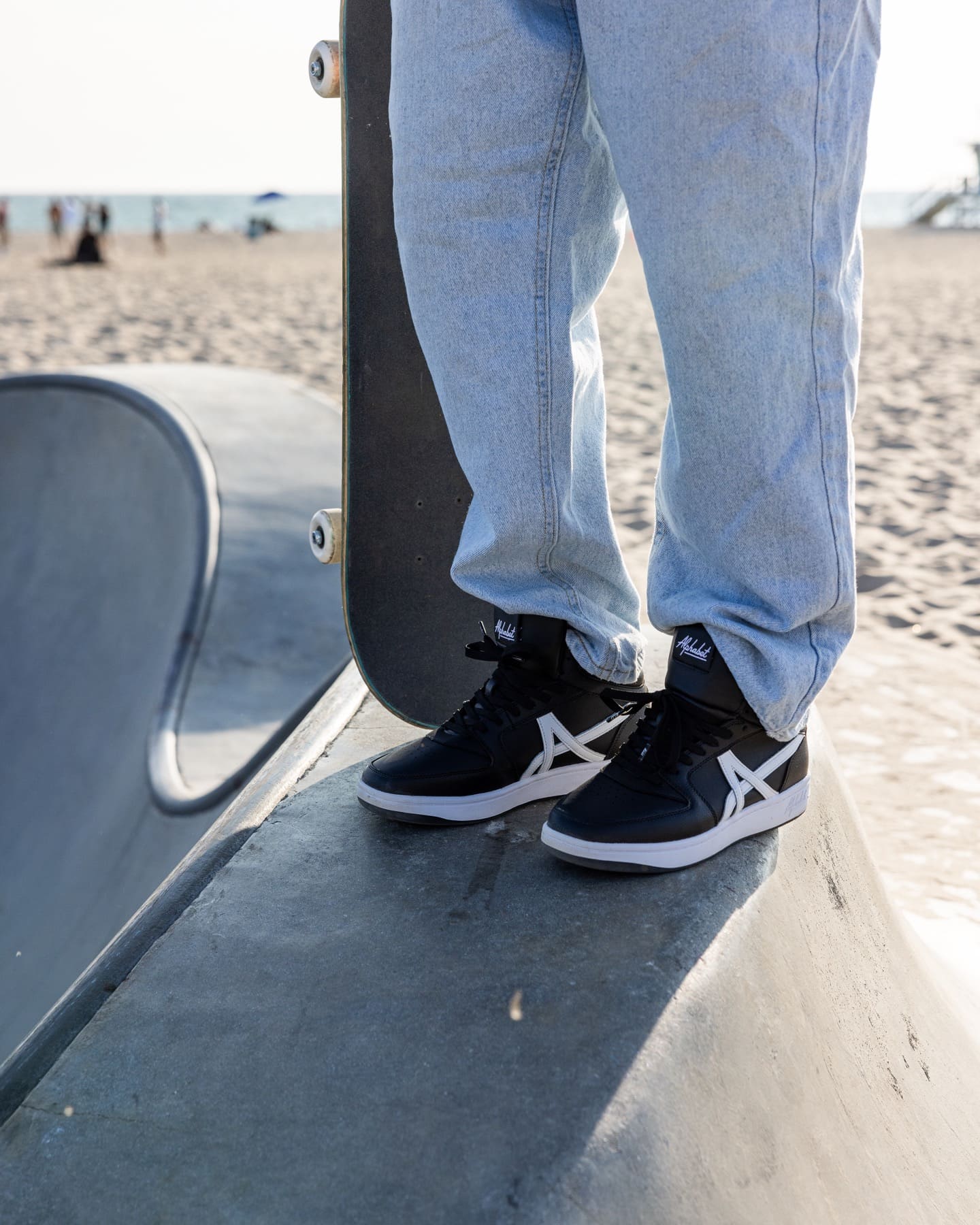 Black high-top sneakers beside a skateboard at the beach